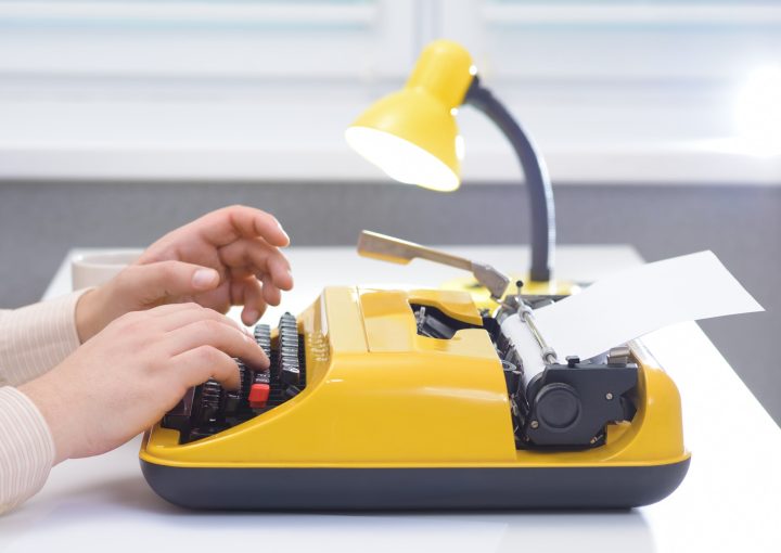 Man typing on yellow typewriter with lamp on white office desk near the window